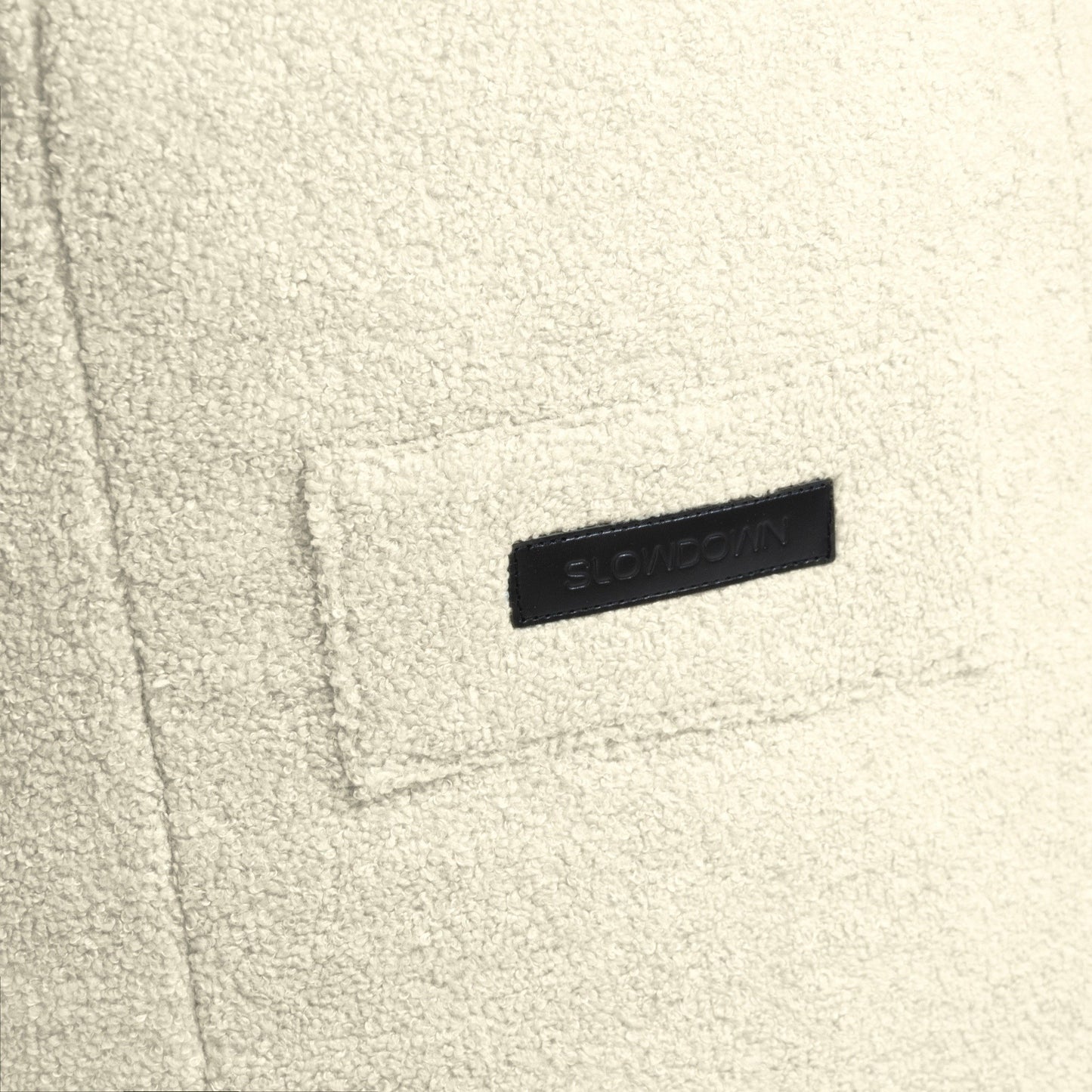 Detalle del tejido texturizado de color blanco roto del puff infantil SNUG 80 TEDDY (80×90×70 cm), con un parche rectangular con la inscripción