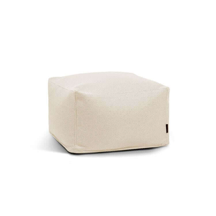 El Pouf Softbox Canaria es una otomana cuadrada beige revestida de tela con tejido extra suave y un diseño sencillo y moderno, ideal para cualquier espacio, incluso al aire libre. Se muestra sobre fondo blanco.