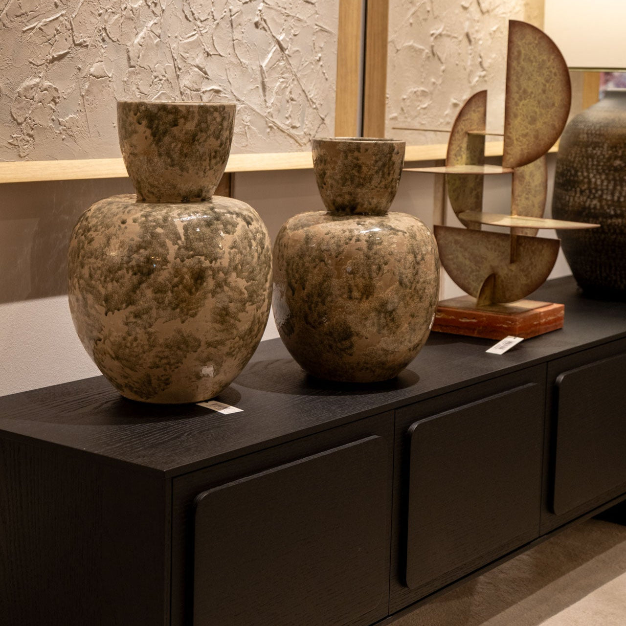 Dos grandes Jarrones en Cerámica Musgo y una escultura abstracta decorativa adornan un aparador de madera oscura contra una pared texturizada, añadiendo un toque único a tu decoración hogar.