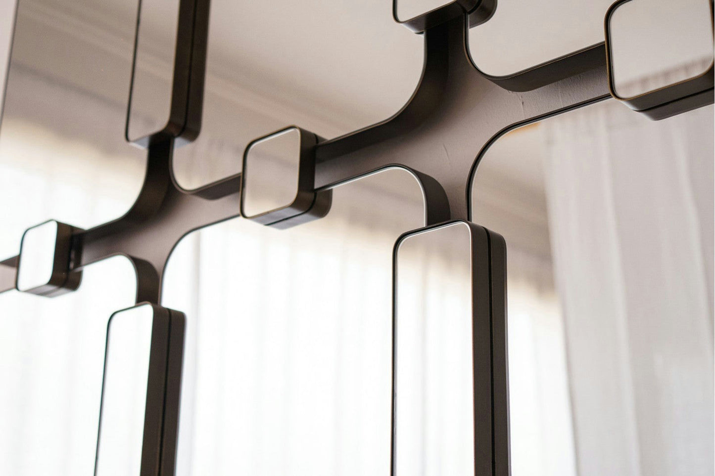 Primer plano del Espejo Rectangular Metálico Industrial Evita, que presenta un marco de metal con múltiples secciones, cortinas transparentes reflectantes y parte de un techo para un toque de diseño moderno.