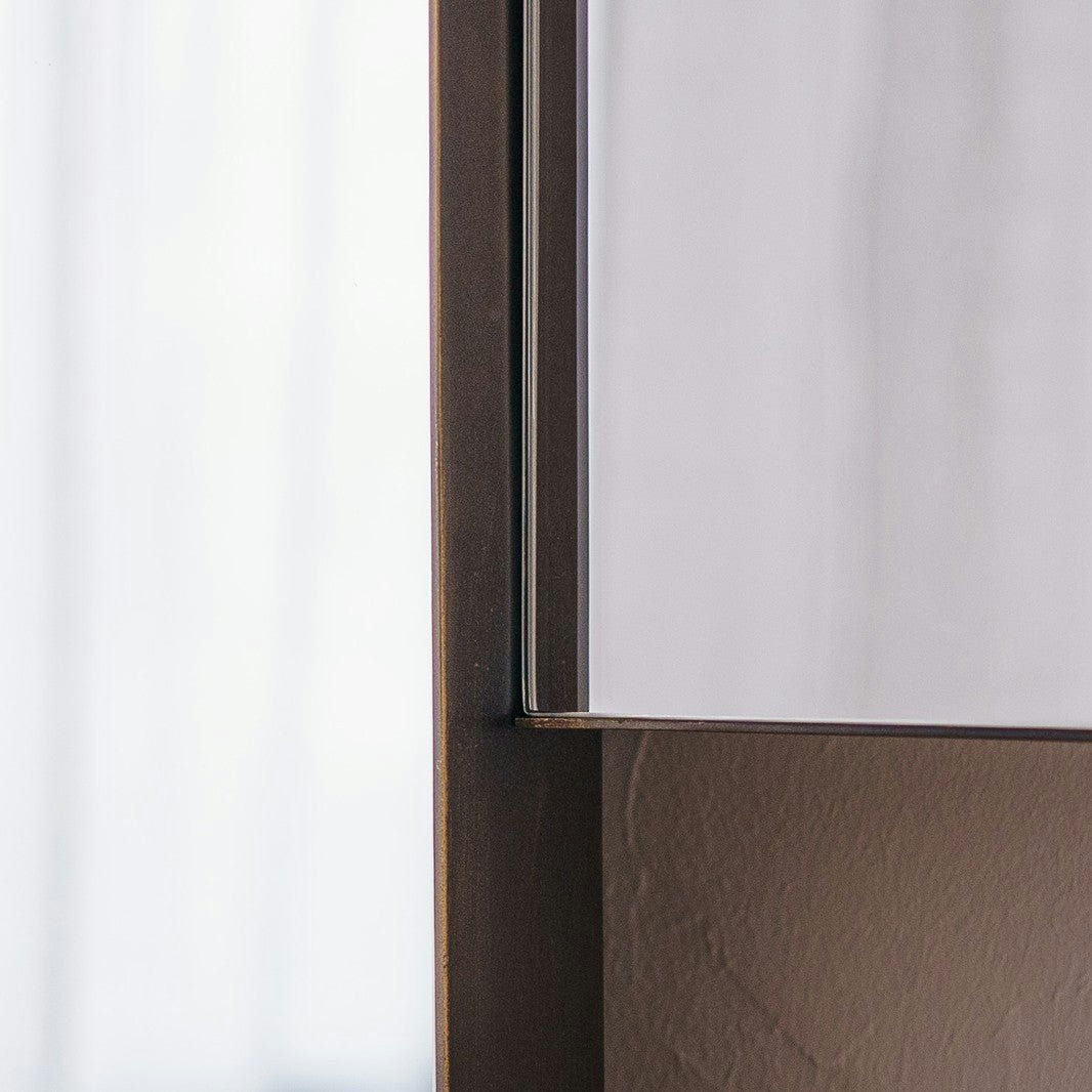 Primer plano de la esquina de un Espejo de Suelo en Metal con Acabado Envejecido N2 rectangular con un delgado marco de metal envejecido, colocado contra una pared de color claro.