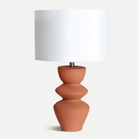 La Lámpara de mesa en cerámica Hasna destaca por su base esculpida y pantalla cilíndrica blanca, ideal para crear una luz suave y sumar un toque atemporal de diseño a cualquier ambiente.