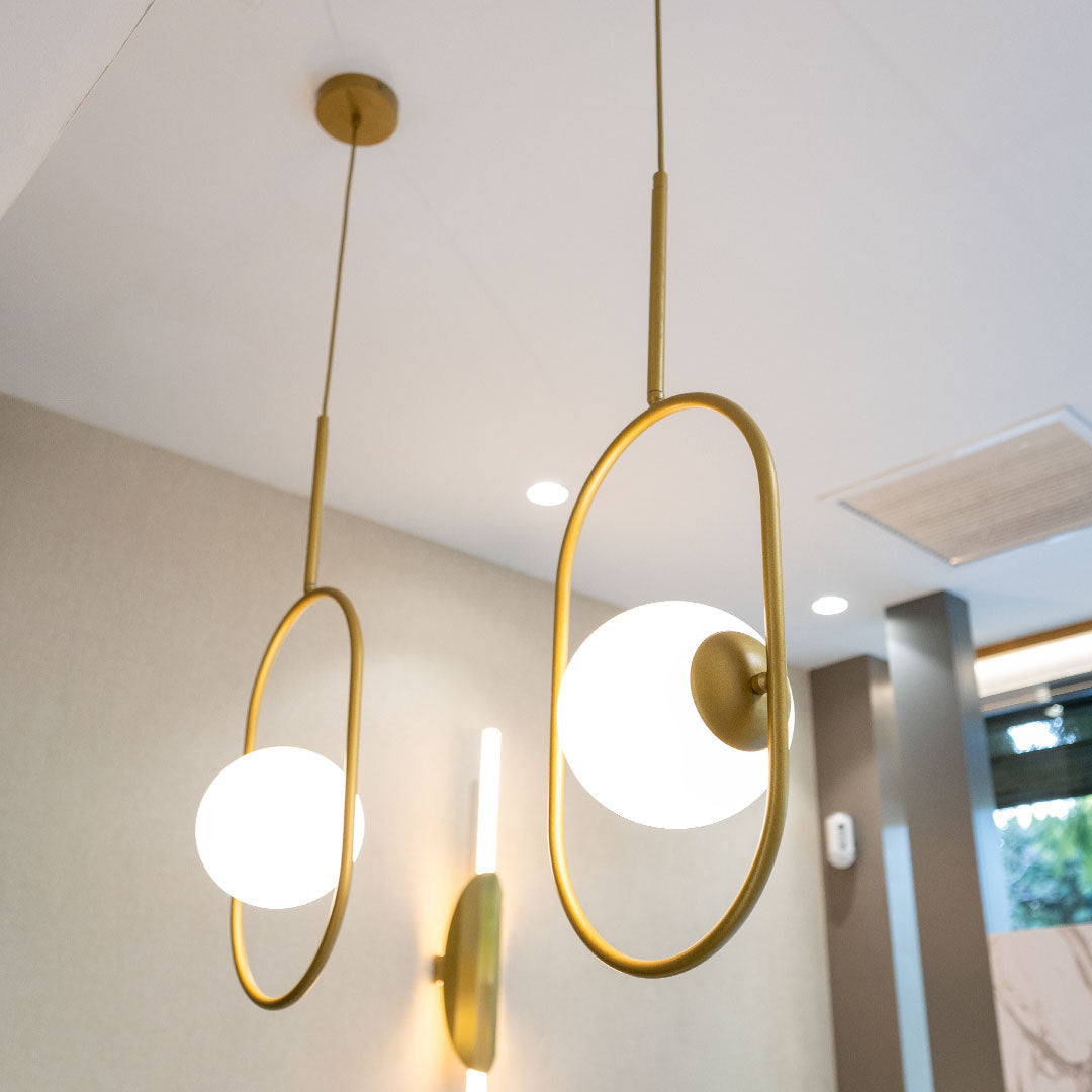 La Lámpara de Techo Colgante Moderna 3135-1C cuenta con dos luces colgantes modernas con marcos de latón ovalados y pantallas esféricas blancas, que ofrecen un diseño industrial-chic que ilumina una habitación con tonos neutros.