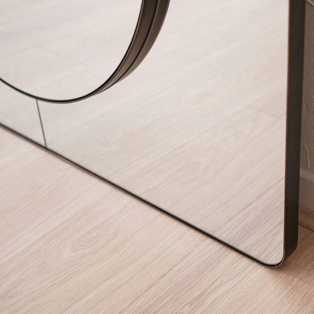 Un primer plano de la esquina inferior de un Espejo de Suelo en Metal con Acabado Envejecido N2, que presenta un recorte circular y un diseño excepcional, colocado sobre un piso de madera clara.