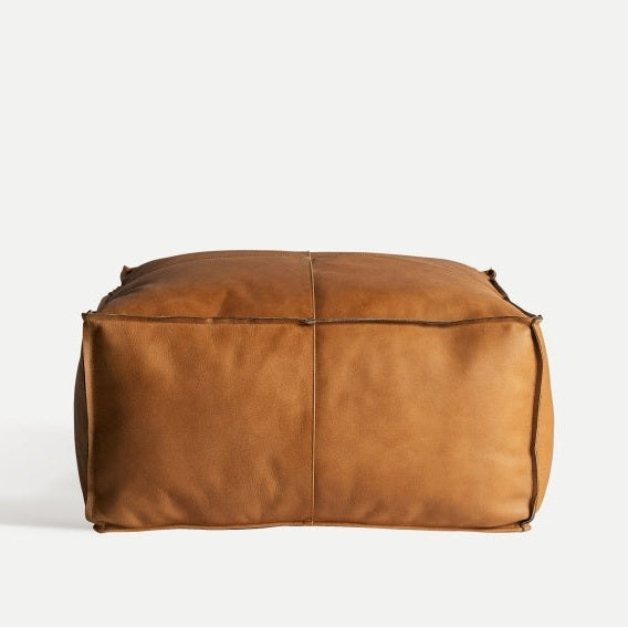 Realza tu espacio con la elegancia del Puff cuadrado en piel marrón Boussac S, bellamente colocado sobre un fondo claro para un asiento adicional ideal.