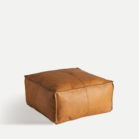 Boussac S, un puf cuadrado de cuero marrón con líneas de costura visibles sobre un fondo liso, es perfecto como asiento adicional.