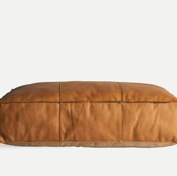 El Puff rectangular de piel marrón con costuras Boussac B presenta costuras visibles, lo que lo convierte en un asiento extra elegante sobre un fondo claro.