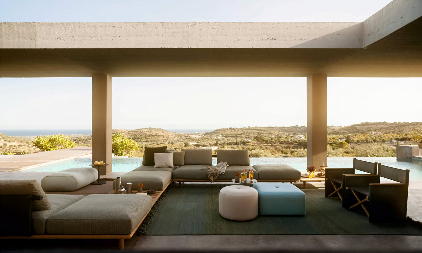 Moderna zona de estar exterior con la Otomana de exterior cuadrado de teca 90 × 90 × 45 cm - moderno - SAMBA, perfecta para relajarse en su terraza con vistas a la piscina y al paisaje bajo un voladizo de hormigón.