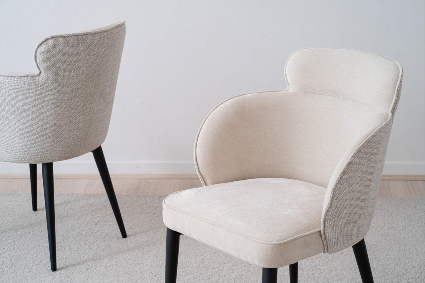 El Pack de 2 Sillas de Comedor Tapizadas con Reposabrazos Oslo en beige y patas negras realza su elegancia y funcionalidad sobre una alfombra gris claro, perfecto para una habitación minimalista.