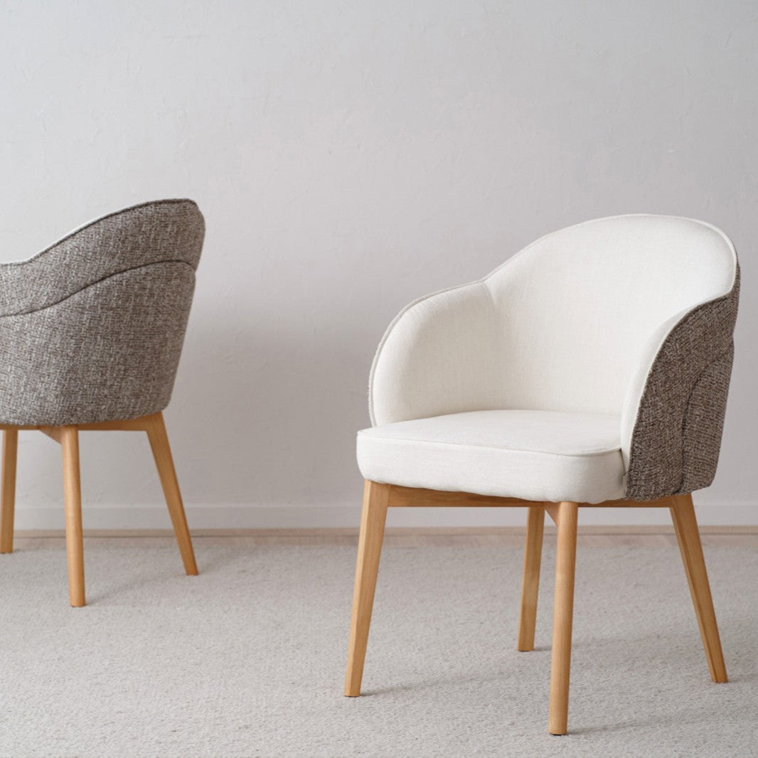 Un paquete de 2 sillas de comedor Roma con patas de madera maciza y cojines beige se asienta elegantemente sobre un piso alfombrado gris, complementando perfectamente la pared gris lisa.