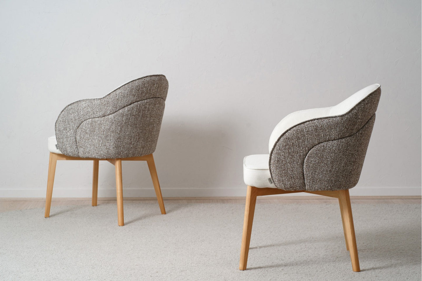 Dos sillas de comedor Roma tapizadas en beige y gris con patas de madera maciza están colocadas sobre un piso alfombrado claro contra una pared blanca lisa.