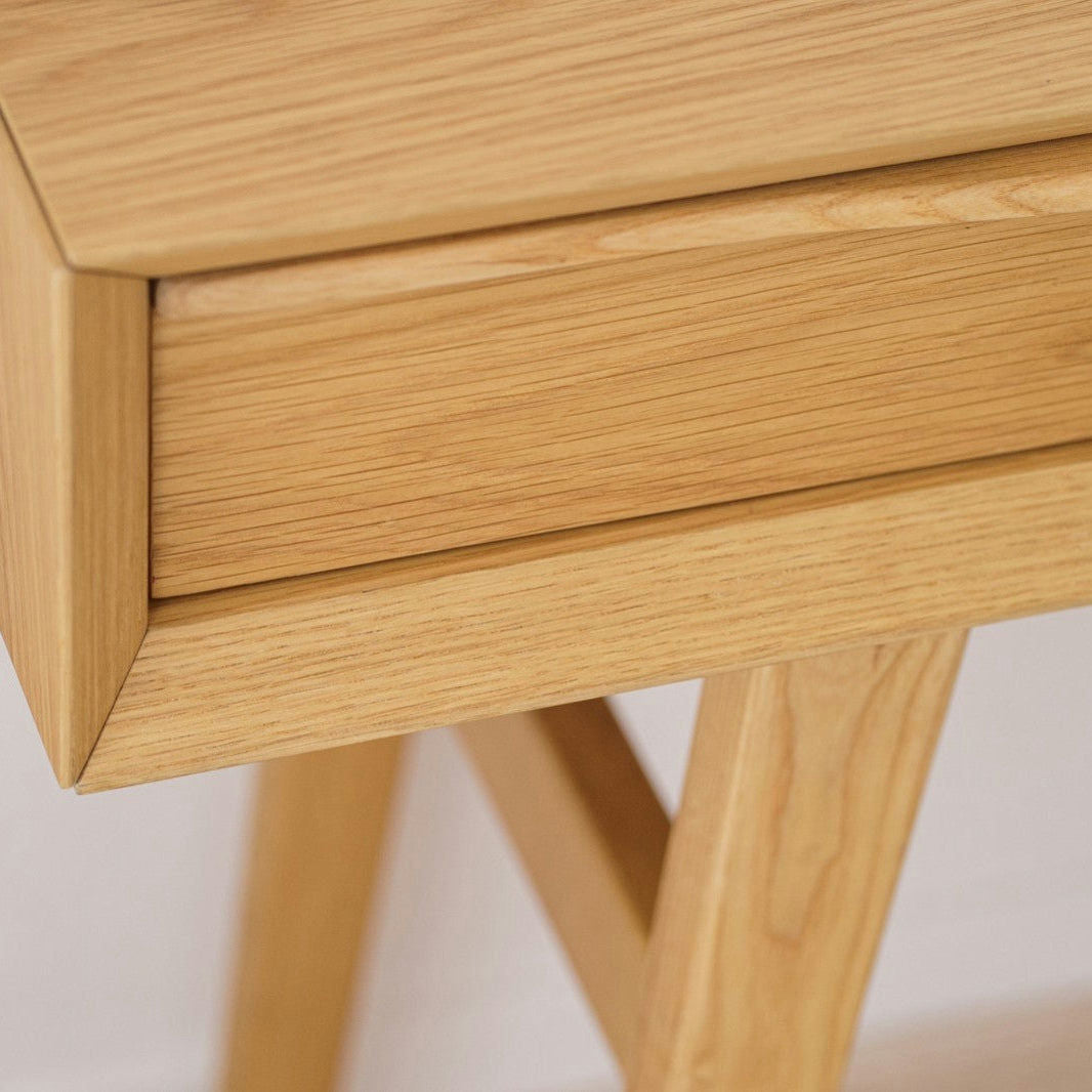 Primer plano de la Consola en Roble Escandinavo Bergen, una mesa o escritorio de madera clara en roble natural con un cajón y patas en ángulo, que enfatiza su diseño escandinavo, veta de madera visible y fina artesanía.