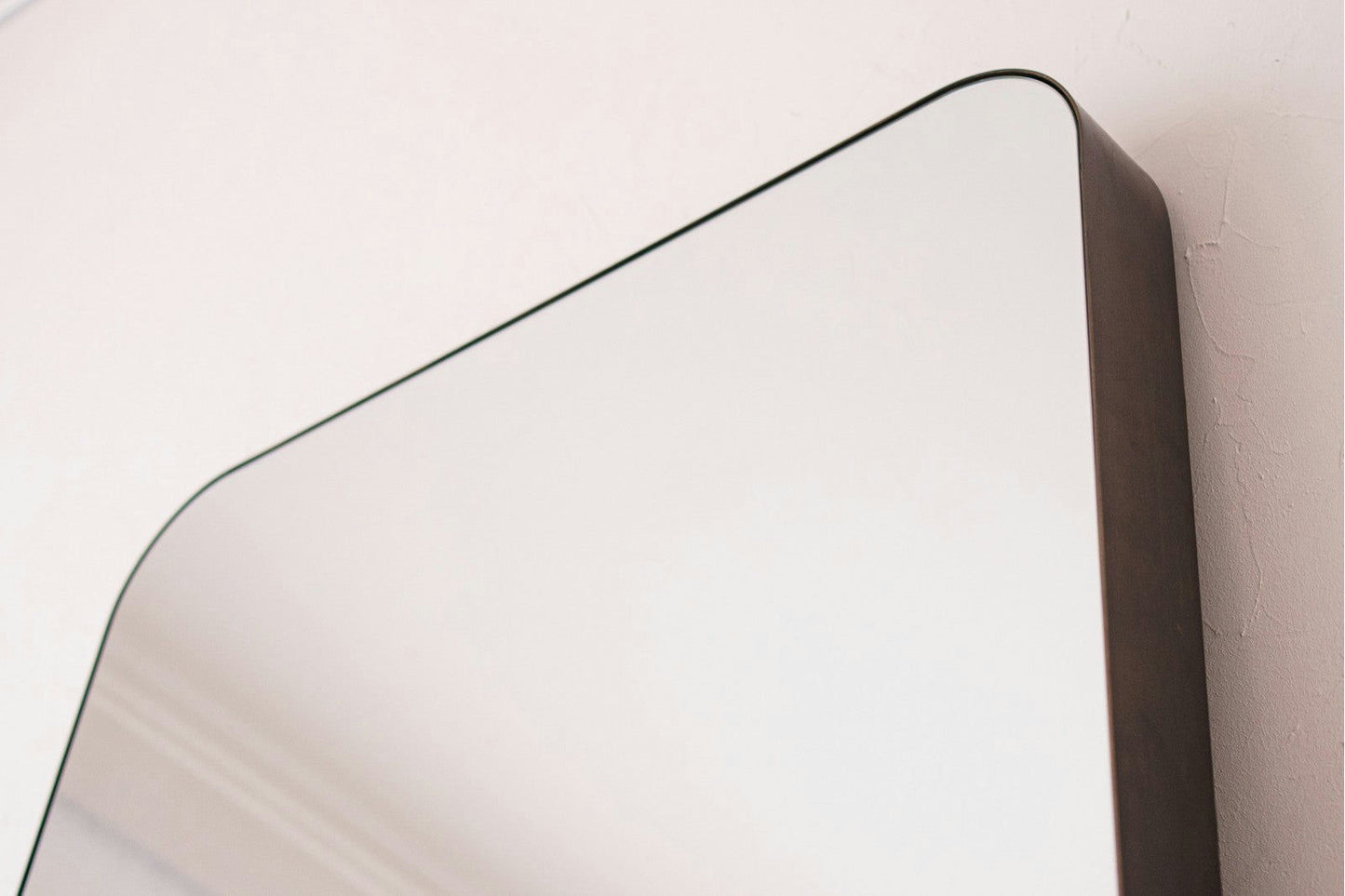 Primer plano de la esquina superior del Espejo de suelo en metal industrial N4, que presenta un marco de metal grueso y oscuro y montado en una pared de color claro.