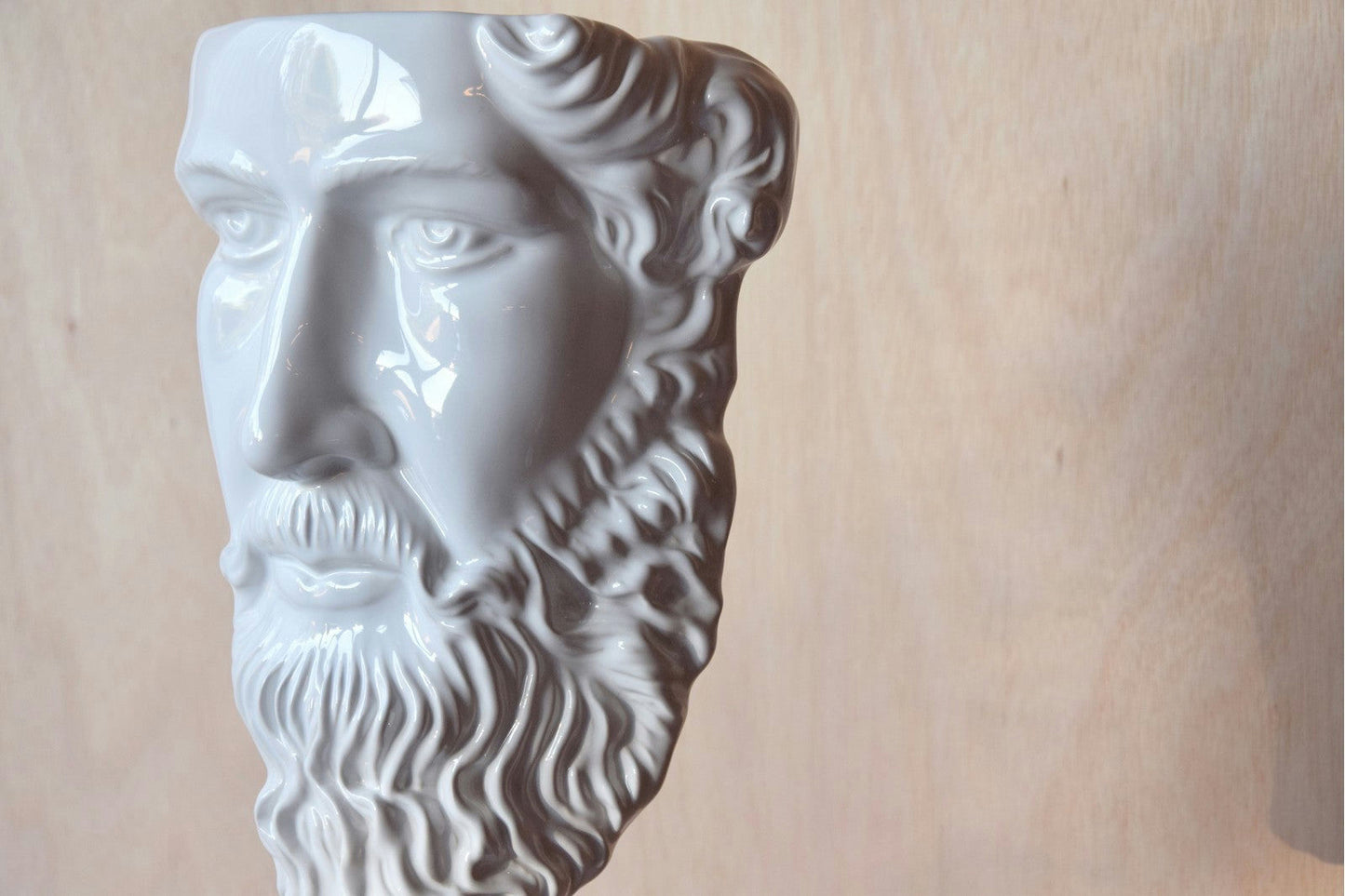 La Figura Decorativa de Cerámica Blanca Griega, con forma de cabeza de hombre barbudo, muestra bellamente el arte clásico reinterpretado sobre un fondo de madera.