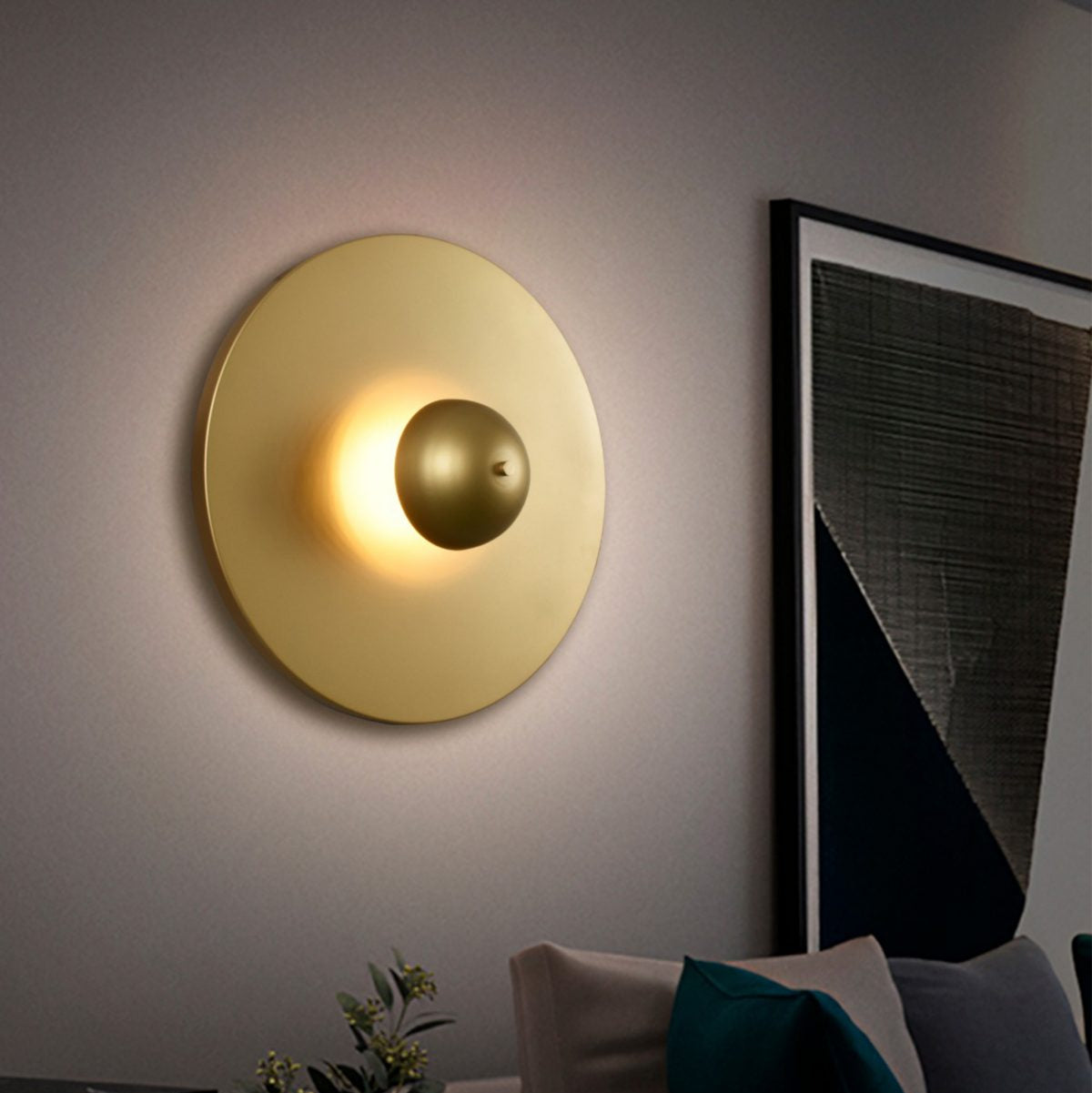 El aplique de pared de acero Disc, con su elegante diseño circular y su lámpara central, realza de forma hermosa un interior moderno. Complementa una obra de arte geométrica enmarcada y un cómodo sofá adornado con cojines.