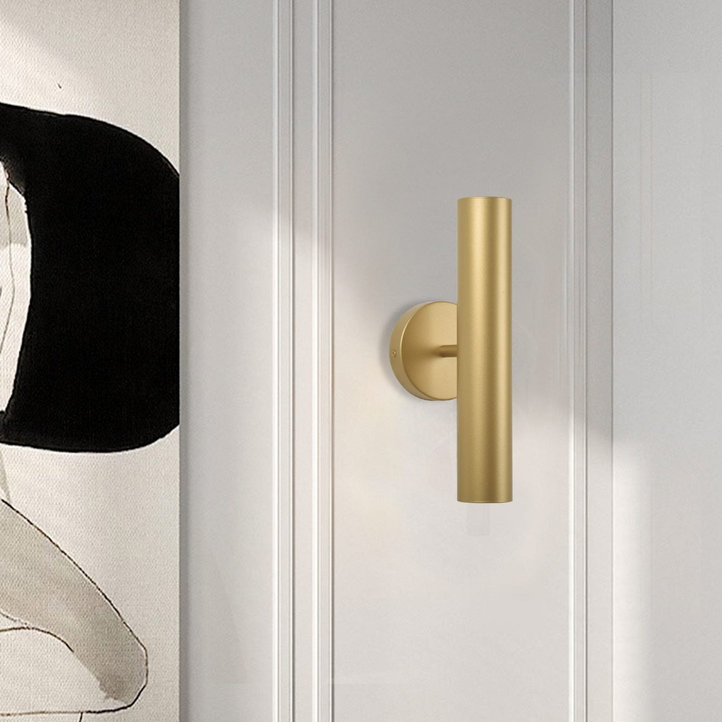 Primer plano de una manija de puerta cilíndrica dorada en una puerta de panel blanco, con parte de un Aplique de pared acero con 2 puntos de Luz Metálica visible en el lado izquierdo, complementando el diseño moderno del espacio.
