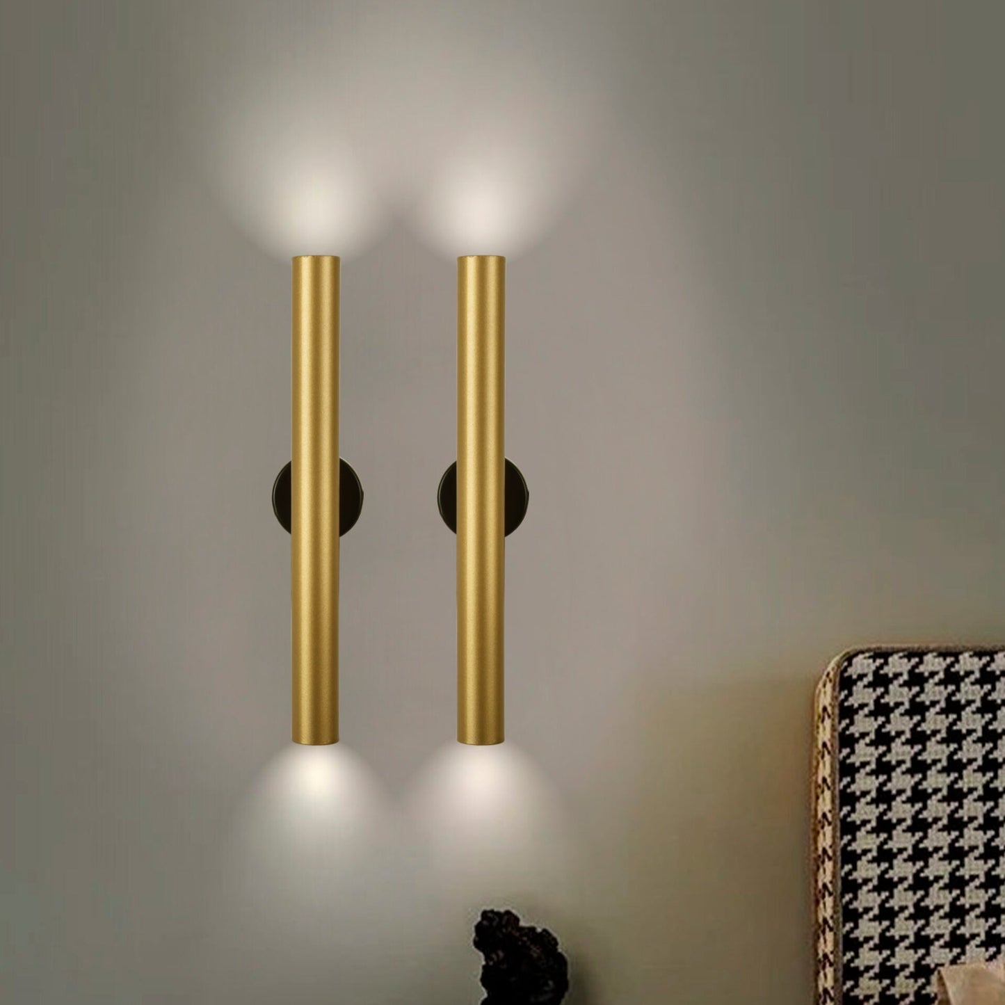 Dos "Aplique de pared en acero con 2 puntos de luz Caia simple" verticales, de diseño moderno e industrial, iluminan una pared gris. En la esquina inferior derecha se ve un mueble estampado.