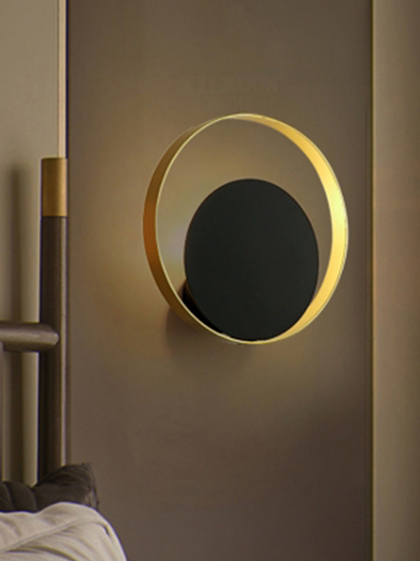 El aplique de pared en acero Echo presenta un diseño redondo y moderno con un anillo dorado y un centro circular negro montado sobre una pared de tono neutro. Este diseño elegante realza cualquier espacio con su iluminación acogedora.