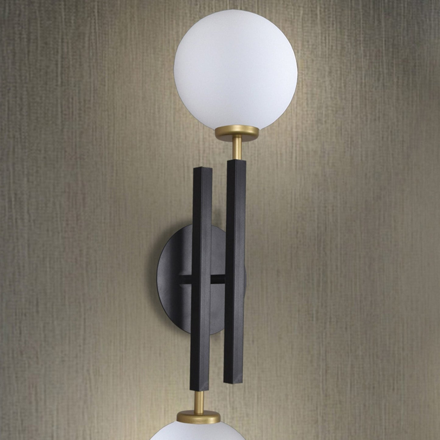 El aplique de pared en acero con 2 puntos de luz Nysa es una moderna luminaria de pared que presenta dos lámparas blancas sobre una varilla vertical negra y dorada, sobre un fondo gris texturizado para crear un ambiente elegante.