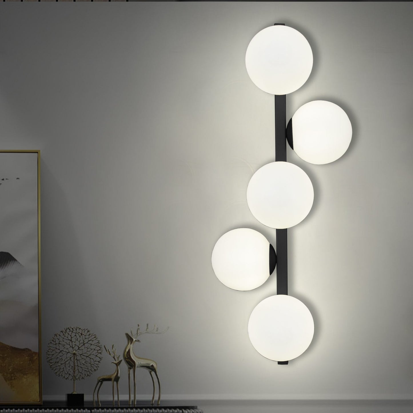 El aplique de pared en acero Holly cuenta con un diseño vertical con cuatro lámparas blancas redondas que se combinan a la perfección con la decoración contemporánea. Complementado con obras de arte abstractas y una figura de ciervo a la izquierda, su elegante acabado en acero negro y dorado agrega elegancia a cualquier espacio.
