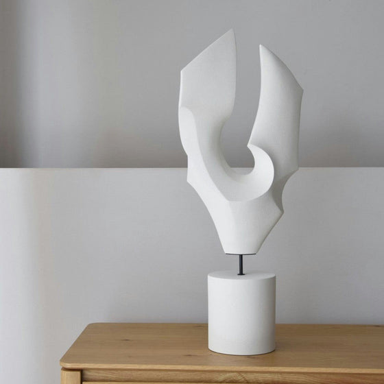 La figura decorativa de cerámica blanca Vento presenta formas geométricas abstractas y curvas y una base cilíndrica. Esta elegante escultura reposa con gracia sobre la madera, encarnando un estilo artesanal moderno.