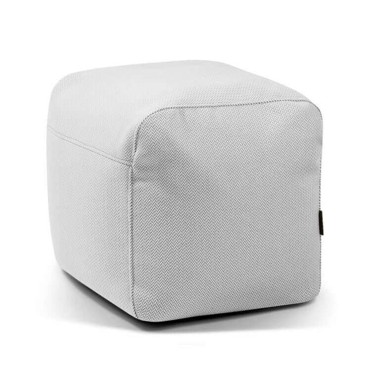 El Pouf Plus 50 Canaria - uso exteriores es un puf gris claro de forma cúbica con bordes redondeados, sutil textura de espiga y una pequeña etiqueta lateral negra, diseñado como un asiento versátil para cualquier espacio.
