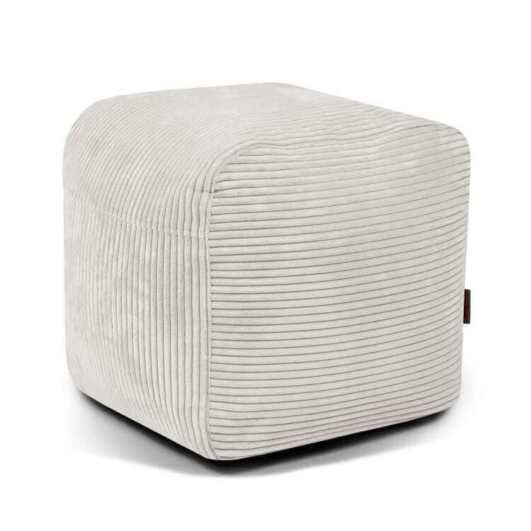 Un puf de terciopelo de pana gris claro, compacto y ligero (PLUS 50 WAVES, 50×50×35 cm), con un moderno diseño acanalado para sentarse cómodamente-perfecto para el dormitorio o el cuarto de juegos-mostrado sobre un fondo blanco liso.