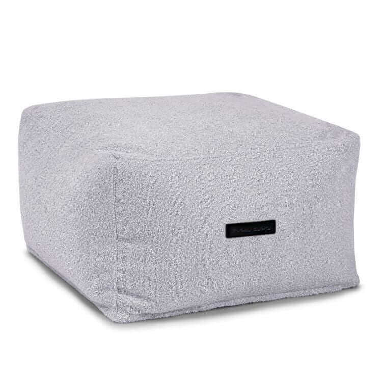 El Puff cuadrado de tejido buclé lavable SOFTBOX MADU (70×70×40 cm) es compacto, gris claro, con costura visible y etiqueta negra, ofreciendo un asiento ergonómico y adaptable para salón o dormitorio.