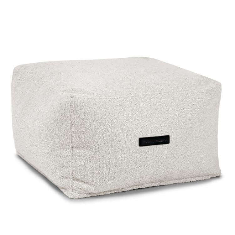 El Puff cuadrado SOFTBOX MADU de tejido buclé lavable (70×70×40 cm), compacto y ergonómico, en color off-white con etiqueta negra lateral, es ideal para salón o dormitorio. Se muestra sobre fondo blanco liso.
