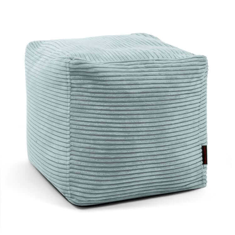 A light blue Puff cuadrado de terciopelo acanalado 45×45×40 cm UP WAVES, compacto y con una pequeña etiqueta negra lateral, ideal como asiento cómodo o reposapiés para dormitorio o salón, sobre fondo blanco.