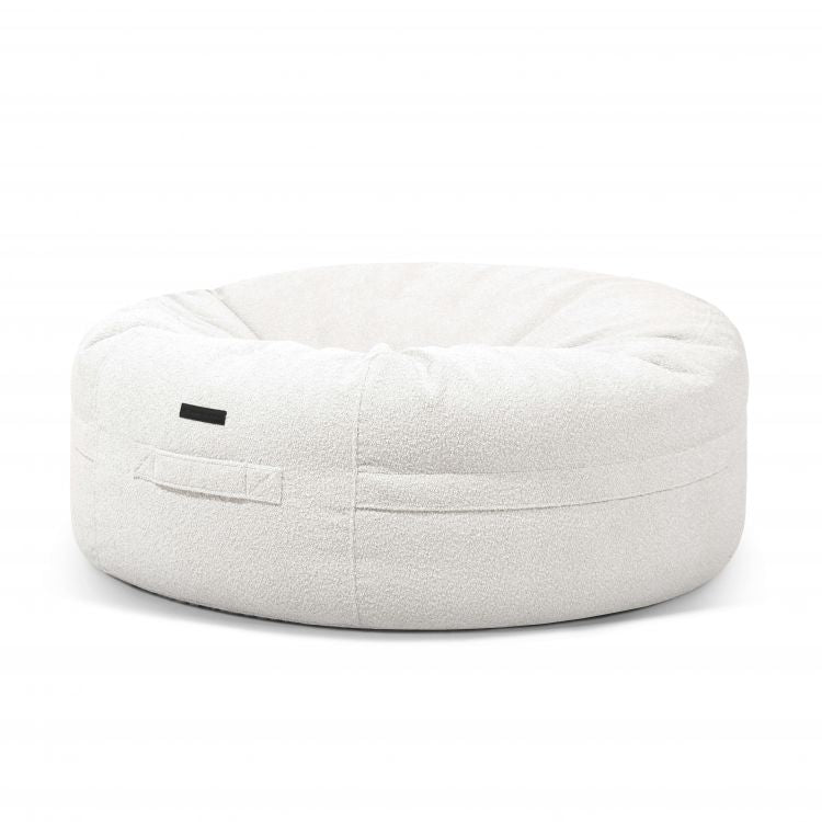 Una gran cama redonda de bouclé blanco para mascotas (135×135×50 cm) llamada ROLL 135 MADU, con una pequeña etiqueta negra y un asa de tela, sobre un fondo blanco.