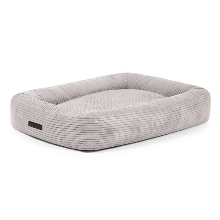 Cama para perro de terciopelo acanalado (100×70×20 cm), rectangular, de color gris claro, con bordes elevados y superficie plana para dormir, sobre fondo blanco.