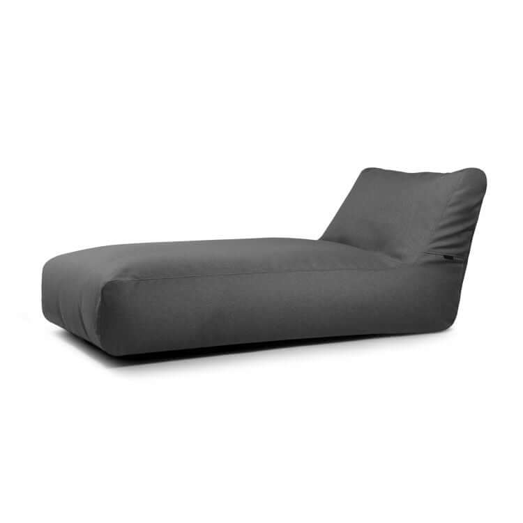 El Bean bag Sunbed 90 Riviera para exterior es una moderna tumbona de tela gris oscuro con perfil bajo y respaldo en ángulo, inspirada en una tumbona ergonómica, que se muestra sobre un fondo blanco liso.