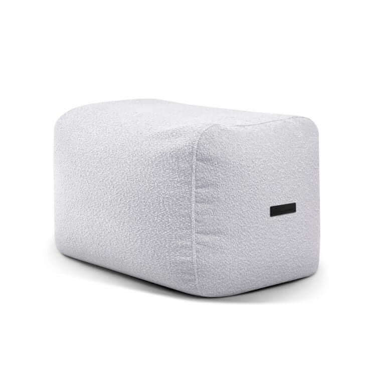 Puf rectangular de tejido bouclé gris claro, compacto y ligero (70×60×45 cm), el modelo PLUS 70 MADU se adapta a dormitorios o salones modernos; se muestra sobre fondo blanco con una pequeña etiqueta negra en un lateral.