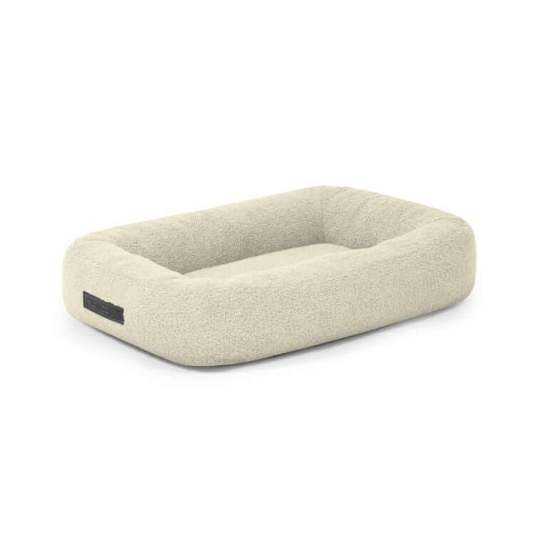 La Cama para perro de tela borreguito 55×45×16 cm - DOG BED 55 TEDDY es una cama rectangular para perros de color beige claro con laterales elevados y una textura suave y afelpada, ideal para la comodidad de su mascota. Se muestra sobre fondo blanco.