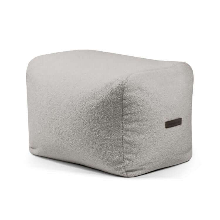 Un Pouf rectangular de tela borreguito compacto y ligero de color gris claro 70×60×45 cm - moderno - PLUS 70 TEDDY con bordes redondeados y una pequeña etiqueta marrón ofrece un apoyo ergonómico para mayor comodidad en su dormitorio o salón.