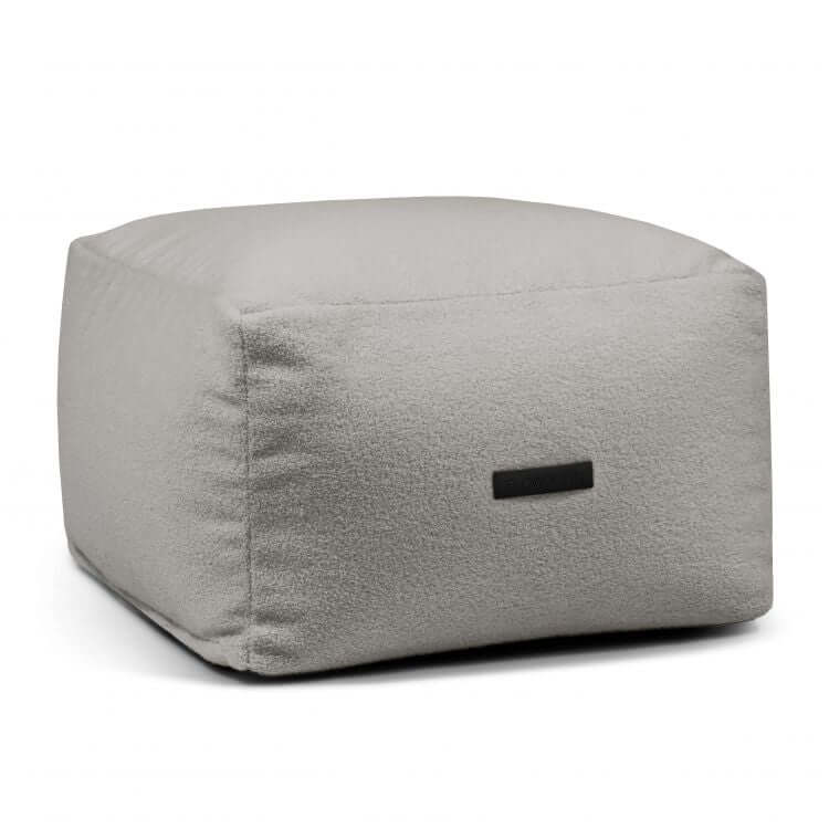 A light gray Puff cuadrado de tejido borreguito lavable 70×70×40 cm - SOFTBOX TEDDY, compacto para salón o dormitorio, con superficie texturizada y pequeña etiqueta negra en un lado, sobre fondo blanco.
