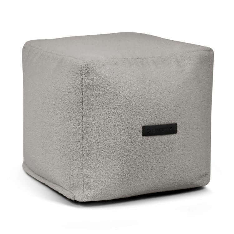 El Puff cuadrado de borreguito UP TEDDY (45×45×40 cm) es un asiento compacto para dormitorio o salón, en color gris claro con funda de tela y etiqueta lateral pequeña, mostrado sobre fondo blanco.