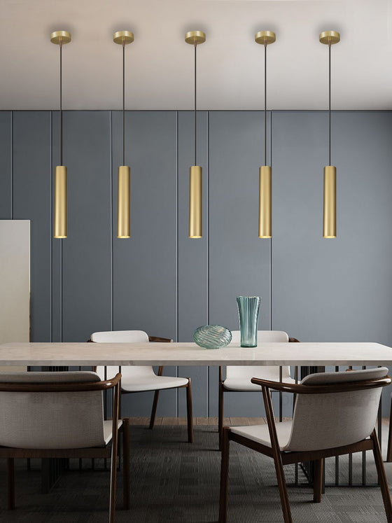 Un comedor moderno cuenta con una mesa de mármol, seis sillas y paneles de pared azules, realzados por la Lámpara de Techo Colgante Dorada 3043-1C-30-3. Estas luces colgantes ofrecen una iluminación cálida y acogedora que agrega elegancia al espacio, mientras que un jarrón y un cuenco de vidrio adornan la mesa.