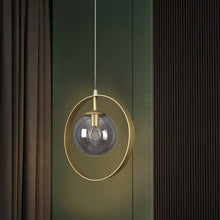  La Lámpara de Techo Colgante Metal Dorado 3222-1C-15-3 ejemplifica la modernidad y elegancia con su marco circular dorado mientras cuelga elegantemente frente a cortinas oscuras, personificando la decoración minimalista y geométrica.