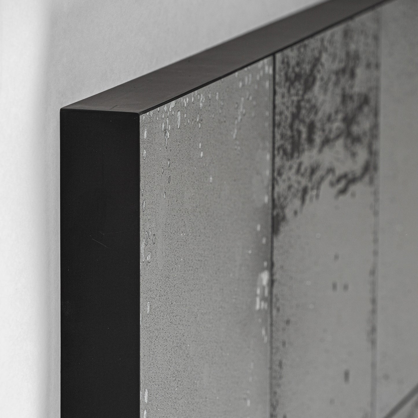 Detalle de la esquina del BOXXI espejo de pared cuadrado de hierro negro 112×4×112 cm, que muestra el desgaste y las manchas de su superficie, colocado contra una pared blanca lisa para un aspecto moderno.