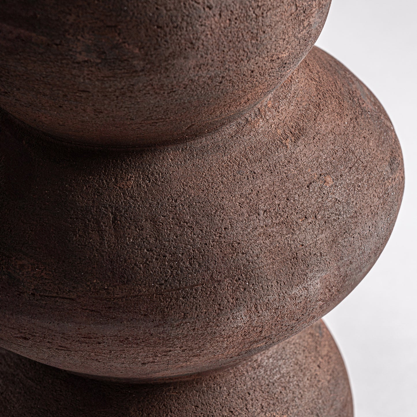 Primer plano de tres formas apiladas y redondeadas que recuerdan al Jarrón en terracota mate 24×24×54 cm - contemporáneo - OKAR G, de material marrón rugoso sobre fondo liso claro.