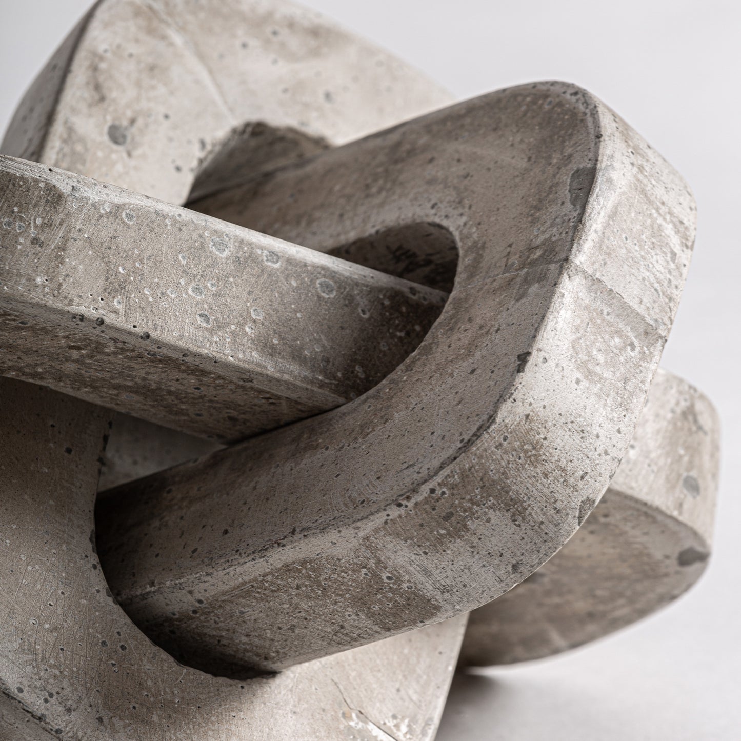 Detalle de la Figura decorativa en cemento y arena 21×21×21 cm - contemporáneo - NEXO: dos formas lisas entrelazadas, de bordes redondeados y textura natural, que reflejan el minimalismo contemporáneo sobre un fondo liso.