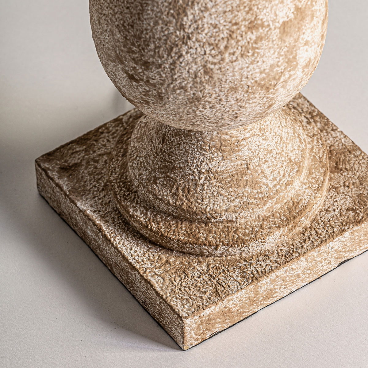 Una esfera de piedra texturizada reposa elegantemente sobre una base cuadrada, evocando el encanto del estilo provenzal sobre una superficie clara en la Lámpara de mesa en resina y yute Provence.