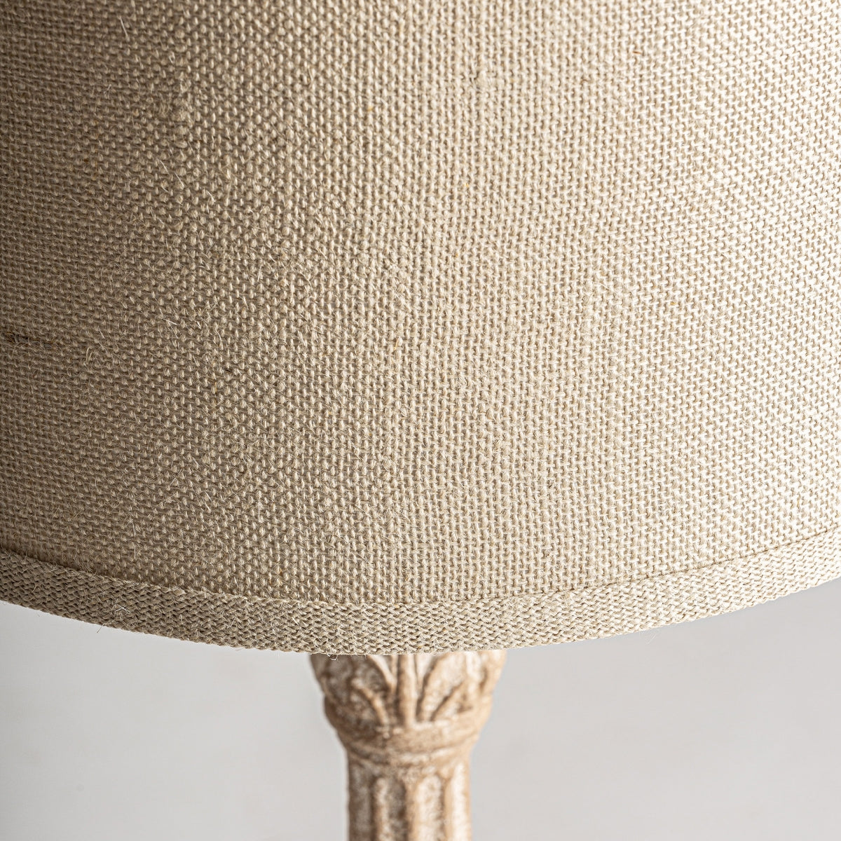 Primer plano de la Lámpara de sobremesa en resina y algodón La pantalla de tela texturizada de color beige de Amira, con parte de su base tallada visible, un ejemplo de diseño atemporal e iluminación elegante.