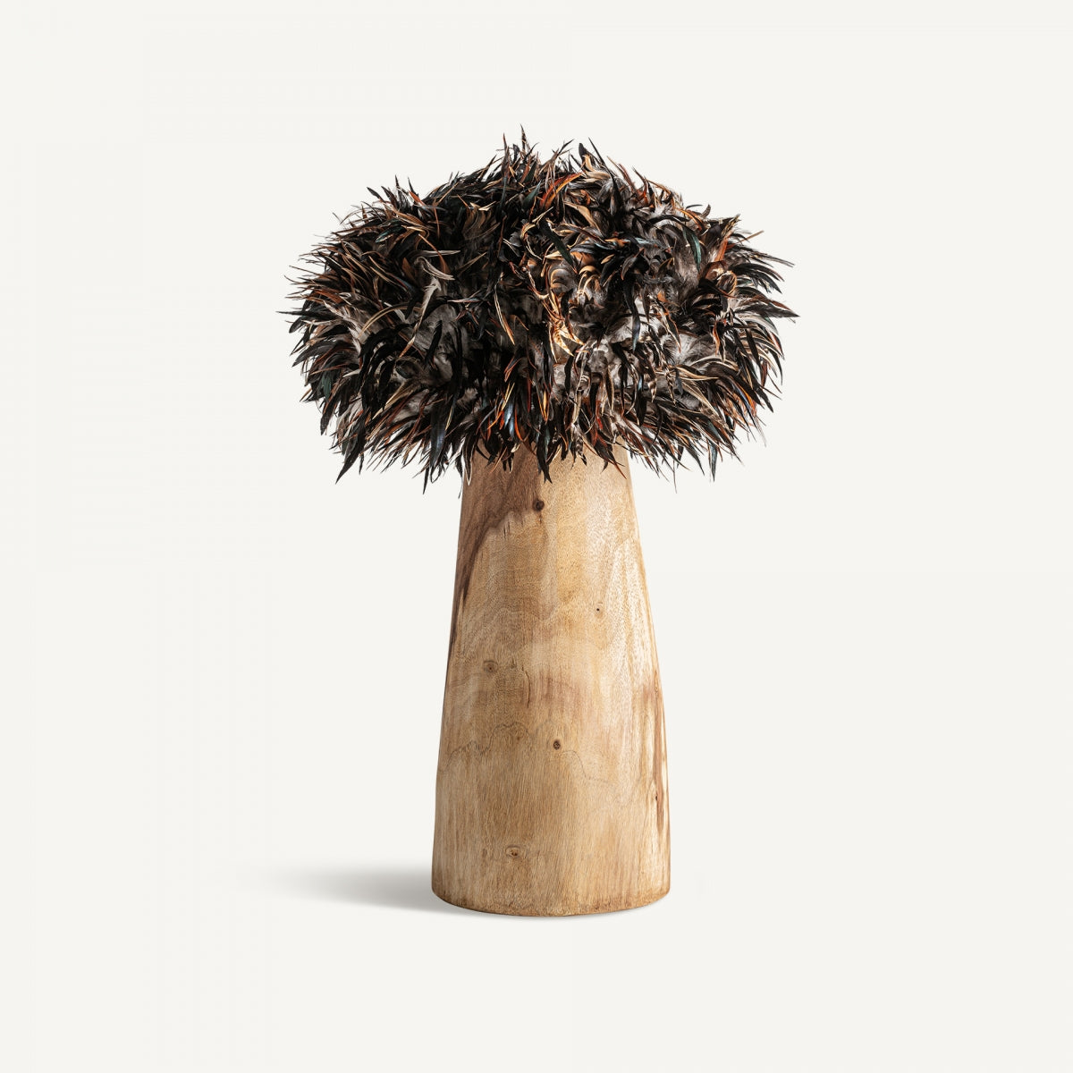 La lámpara de mesa en teka y plumas Ghedas presenta una base cónica de madera de teca rematada con plumas oscuras y puntiagudas, creando una lámpara de mesa atrevida y original sobre un fondo blanco liso.