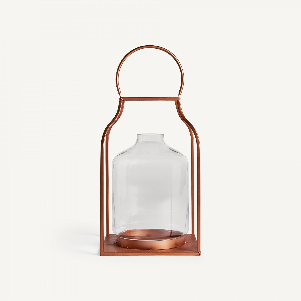 El Faro de vidrio y acero cobre es un recipiente de vidrio con marco metálico color cobre y asa superior, similar a una linterna industrial. Ideal para crear efectos de iluminación cálidos, se presenta sobre un fondo blanco.