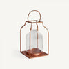 El Farol en vidrio y acero cobre Faro cuenta con una linterna de vidrio en un marco de metal de color cobre, completa con una base cuadrada y un mango redondeado, que agrega una iluminación cálida a cualquier espacio.