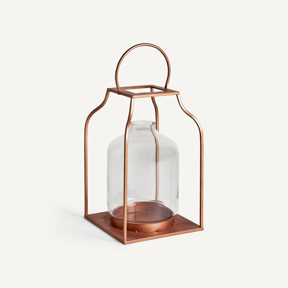 El Farol en vidrio y acero cobre Faro cuenta con una linterna de vidrio en un marco de metal de color cobre, completa con una base cuadrada y un mango redondeado, que agrega una iluminación cálida a cualquier espacio.