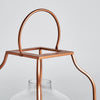 El Farol en vidrio y acero cobre Faro es una linterna de metal de color cobre con parte superior cuadrada y asa arqueada, vidrio transparente en la parte inferior y acabado industrial, ideal para agregar una iluminación cálida a cualquier espacio.